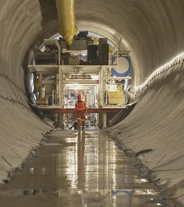 Man sieht einen Tunnel an dessen Ende ein Bauarbeiter an einer Konstruktion steht