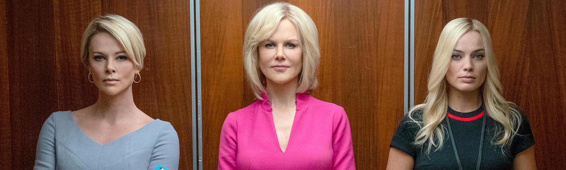 Drei Frauen in Etuikleidern stehen nebeneinander in einem offenen Fahrstuhl und blicken den Betrachter an. Die Frau in der Mitte, Gretchen Carlson (Nicole Kidman) trägt ein auffälliges, pinkfarbenes Kleid.