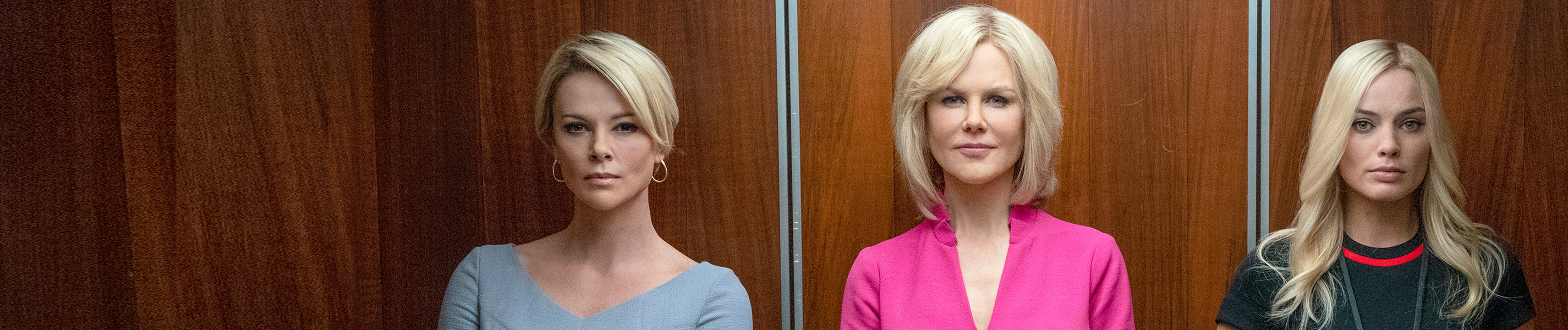 Drei Frauen in Etuikleidern stehen nebeneinander in einem offenen Fahrstuhl und blicken den Betrachter an. Die Frau in der Mitte, Gretchen Carlson (Nicole Kidman) trägt ein auffälliges, pinkfarbenes Kleid.