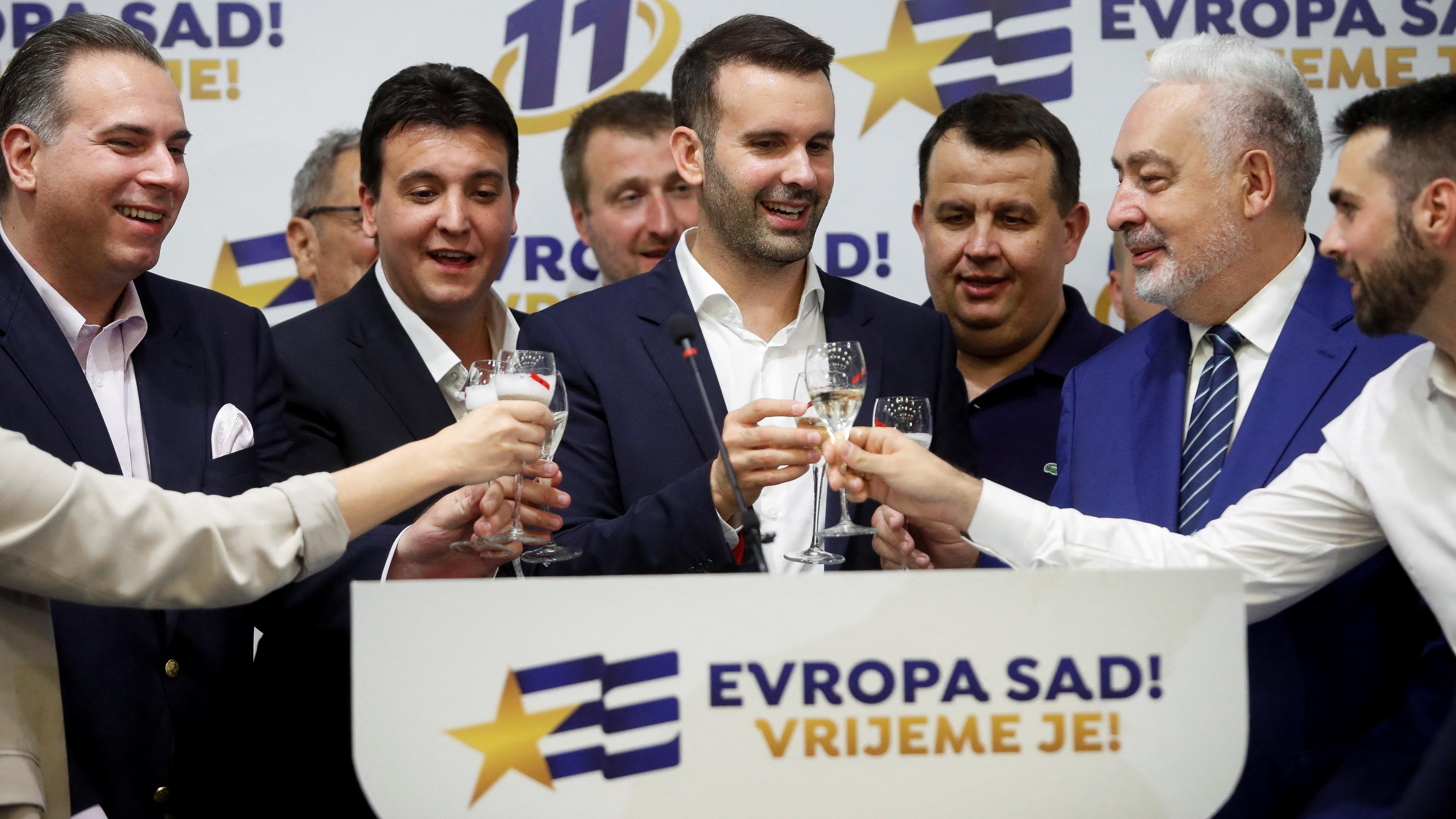 Milojko Spajic und Unterstützer stoßen an, im Hintergrund ist das Logo der Partei "Europa Jetzt!" (PES) zu sehen.