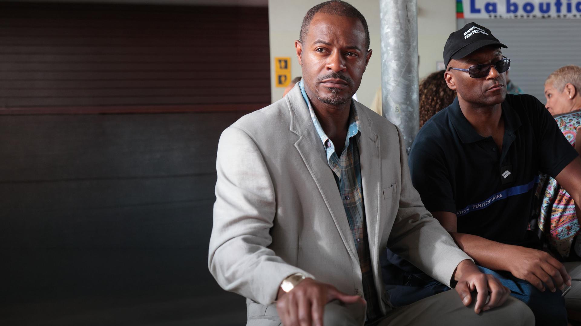 "Death in Paradise - Mord an Bord": Leon Hamilton (Jeff Alexander) und der Gefangene Vincent Carter (Colin Salmon) sitzen in einem Wartebereich.