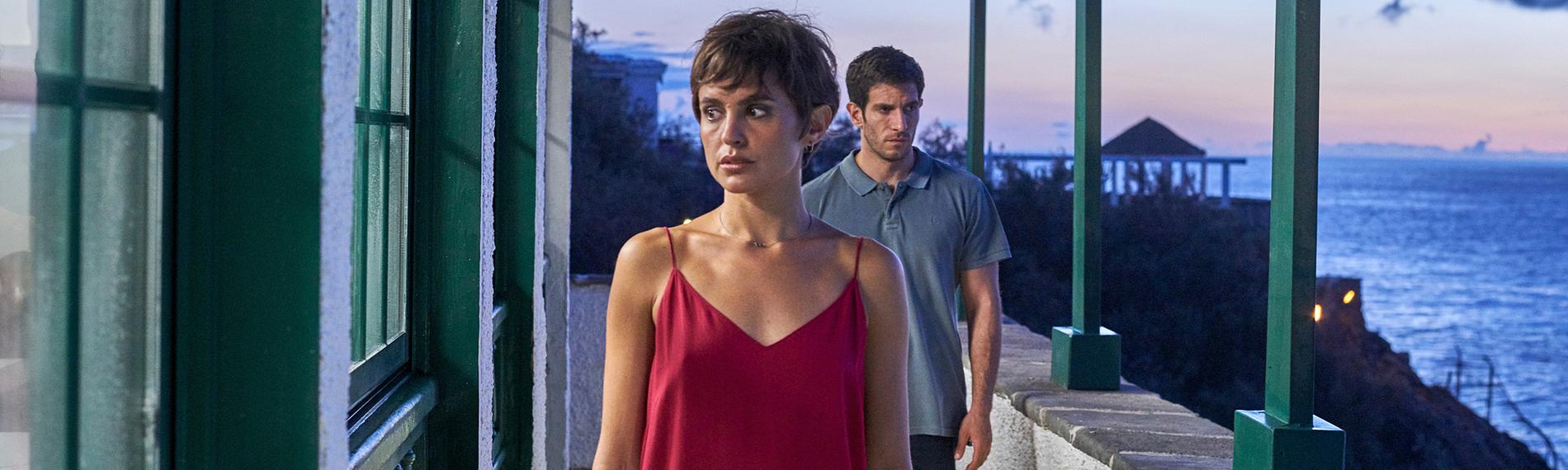 Ruth Anglada (Verónica Echegui) steht auf einem Balkon mit Meeresblick, hinter ihr nähert sich Sargento Bevilacqua (Quim Gutiérrez).