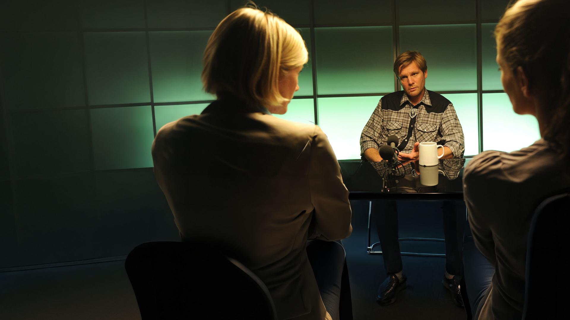 Martina Seiffert (Astrid M. Fünderich) und Selma Kirsch (Yve Burbach) sitzen Bastian Hölzner (Kai Ivo Baulitz) im Vernehmungsraum gegenüber. Hölzner blickt entspannt zu Martina.