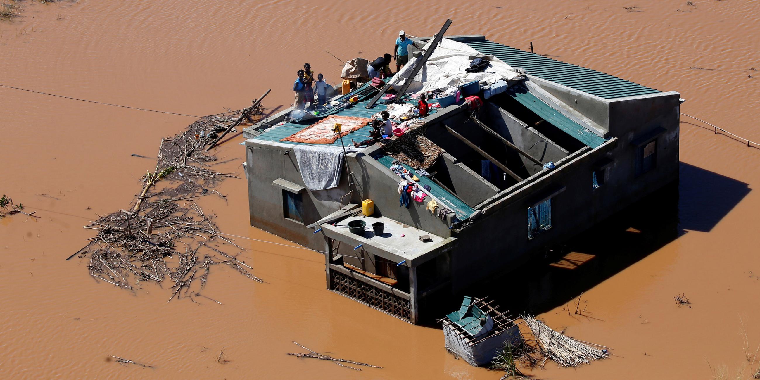 Überschwemmte Landschaft und Menschen, die auf einem Dach Zuflucht suchen am 18.03.2019 in Mosambik