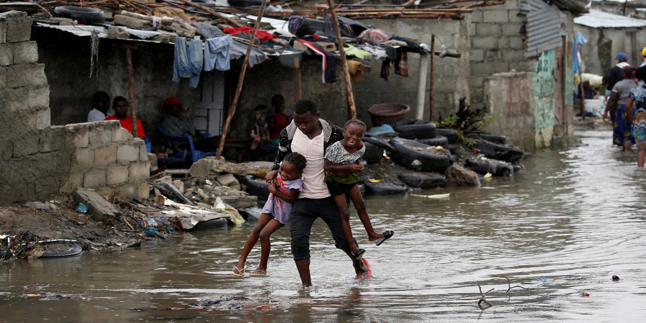 Ein Mann trägt zwei Kinder durch überflutete Straßen am 23.03.2019 in Mosambik