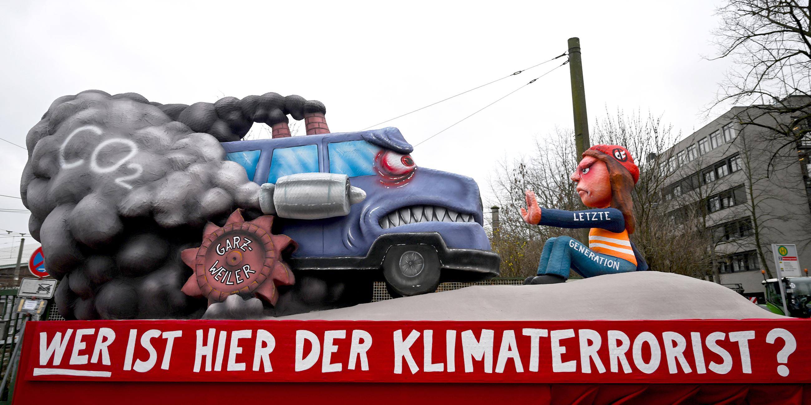 Ein Mottowagen mit der Aufschrift "Wer ist hier der Klimaterrorist?" zeigt einen Aktivisten der letzten Generation und ein qualmends Auto.