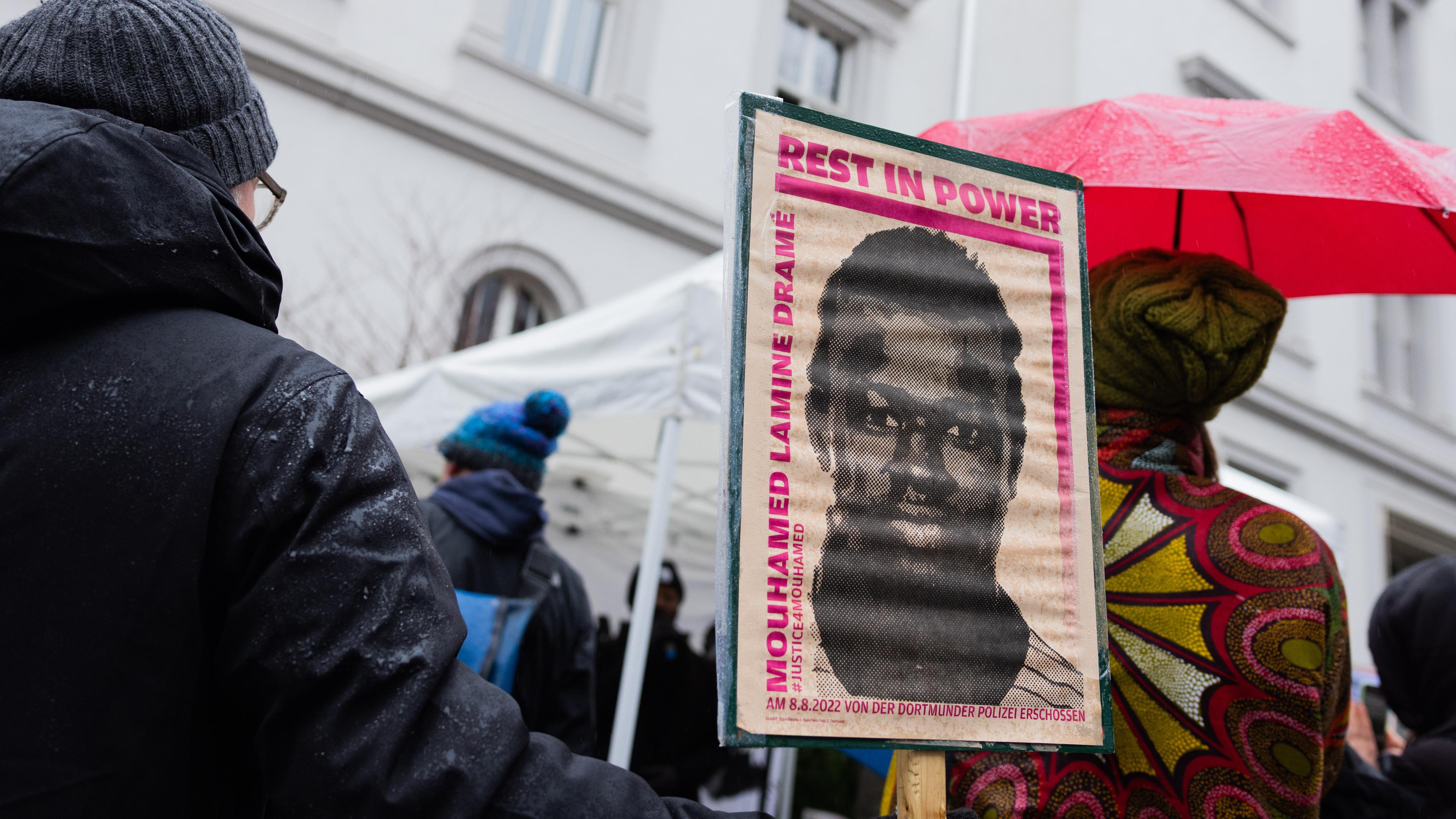 Demonstranten stehen mit Plakaten, die das Portrait des 16-jährigen Senegalesen Mouhamed Drame zeigen, vor dem Landgericht in Dortmund am 19.12.2023.