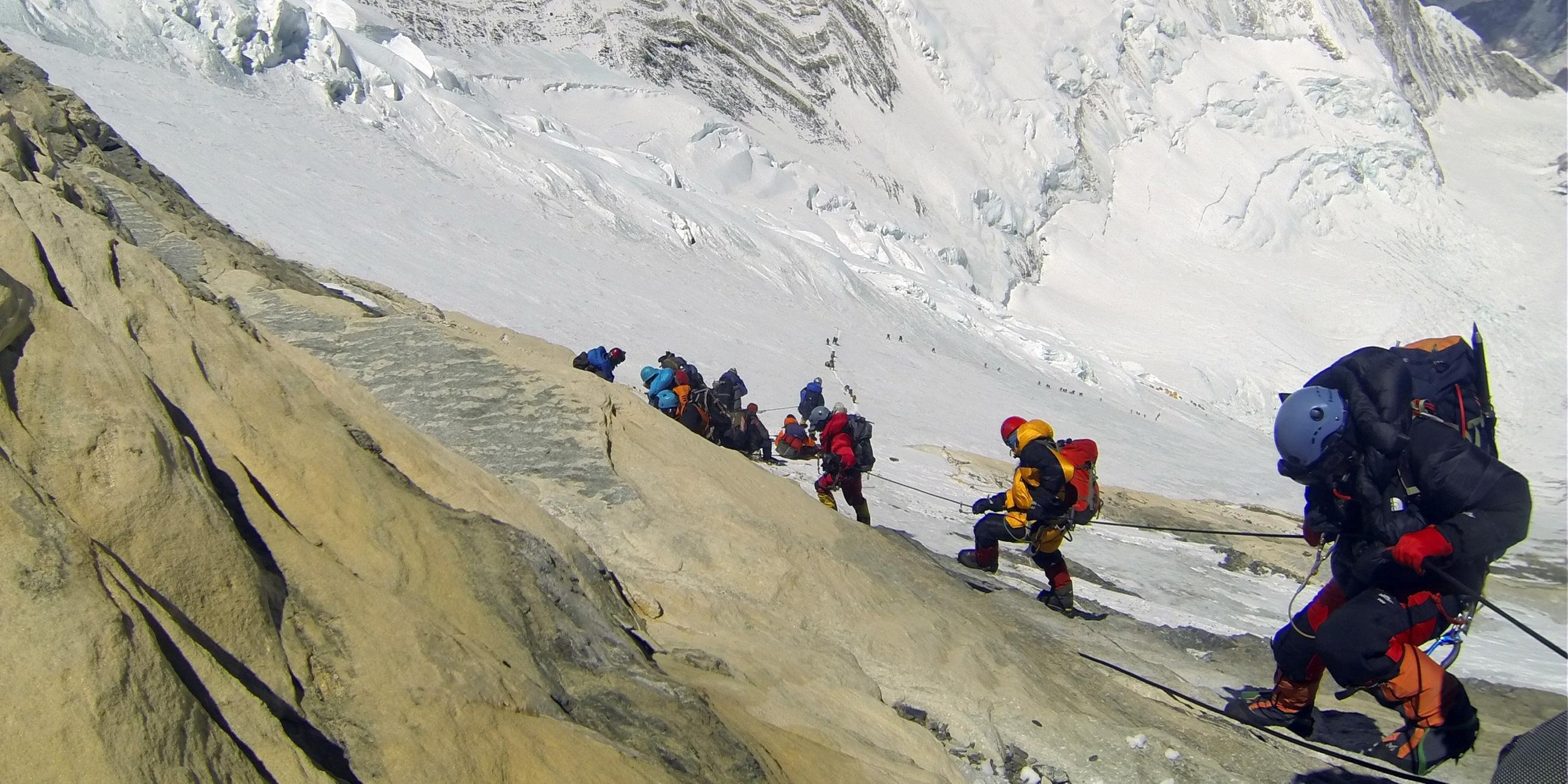 Mehre Menschen in bunter Bergsteiger Ausrüstung erklimmen den schneebedeckten Mound Everest.
