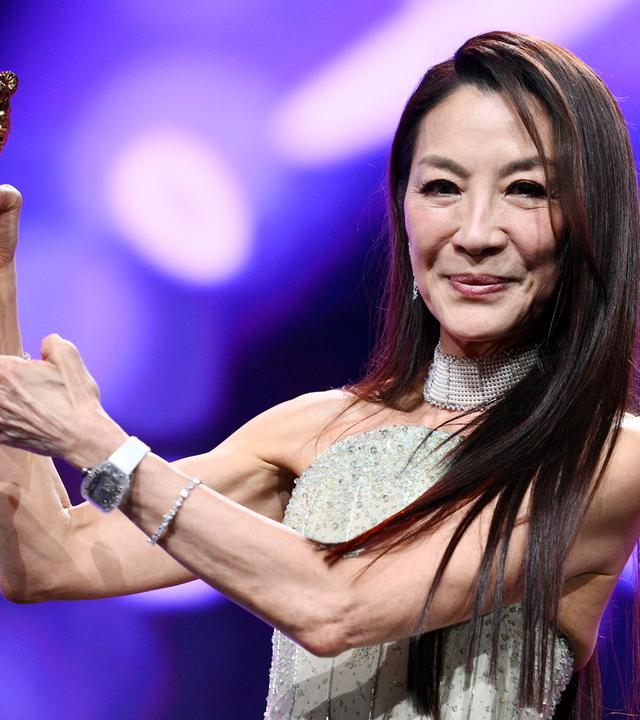 Frau hält Preisstatuette in Form eines goldenen Bären in den Händen und lächelt