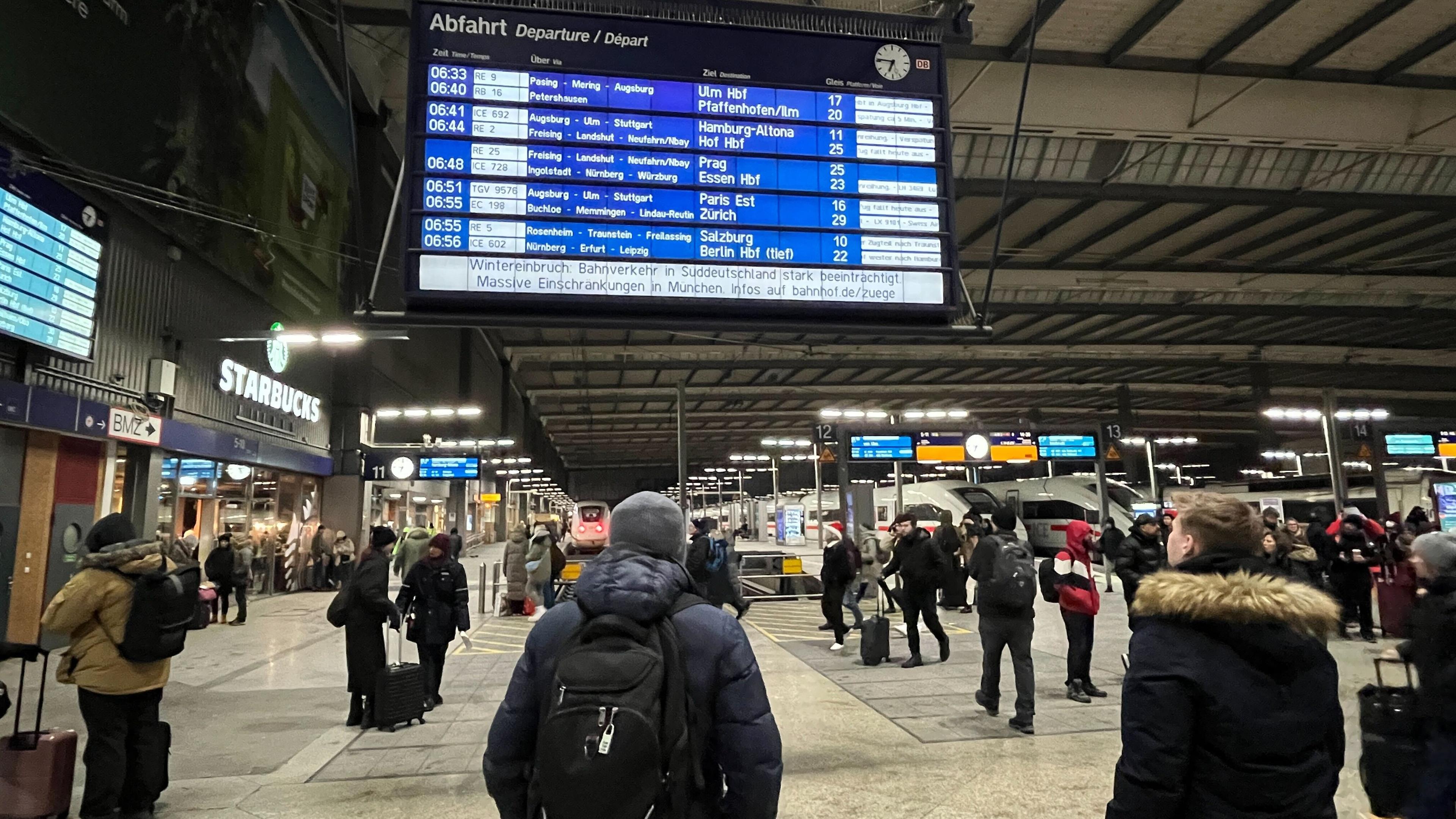 Reisende in Witnerkleidung stehen vor einer Anzeigetafel im Hauptbahnhof München