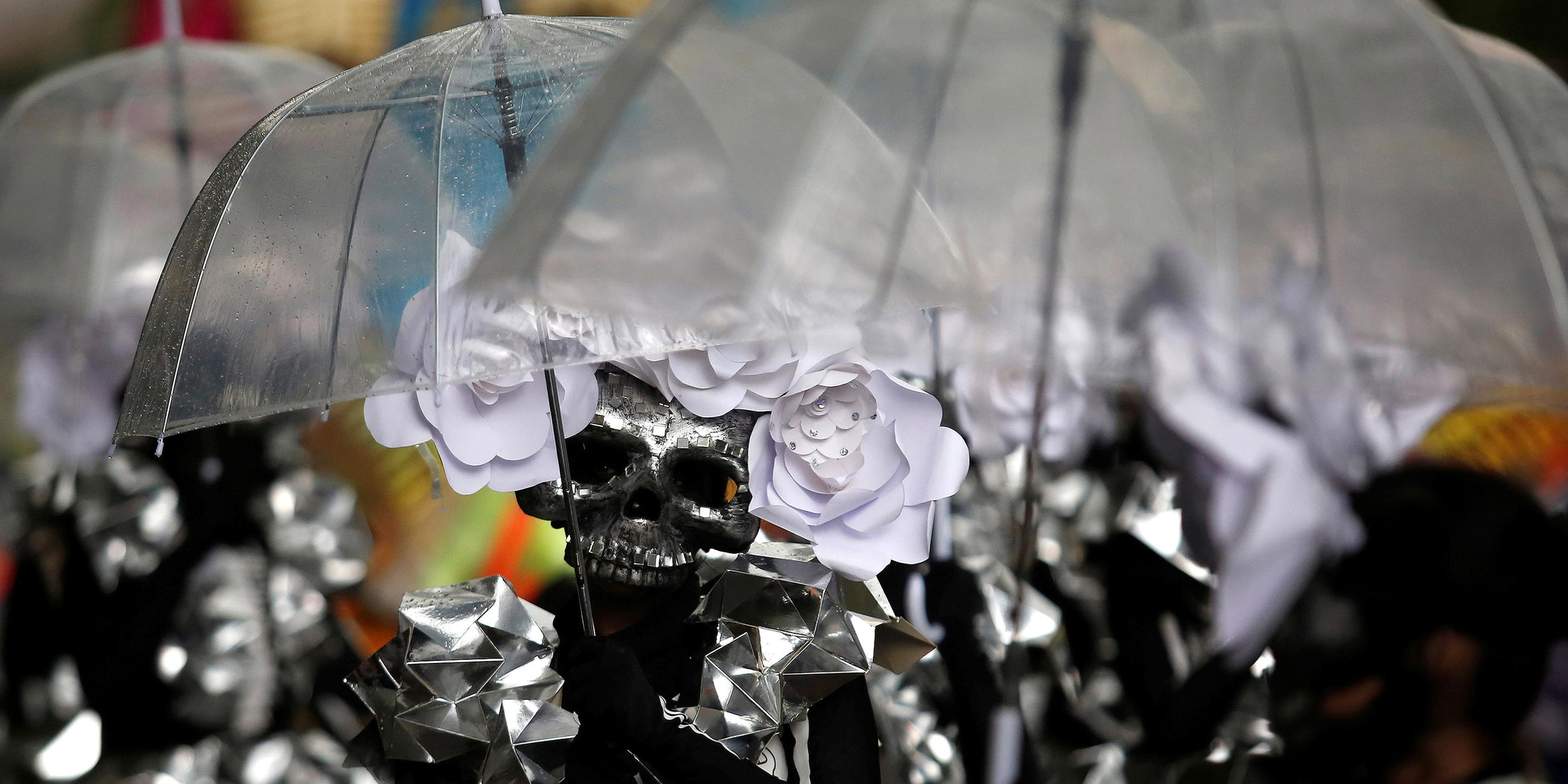 Eine Gruppe mit Totenkopfmasken unter Regenschirmen beim day of the dead in Mexiko City