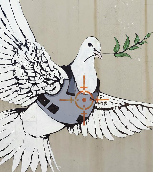 Auf eine Wand ist eine Friedenstaube mit Schutzweste und Zielkreuz auf der Brust gemalt, die einen Olivenzweig im Schnabel trägt.