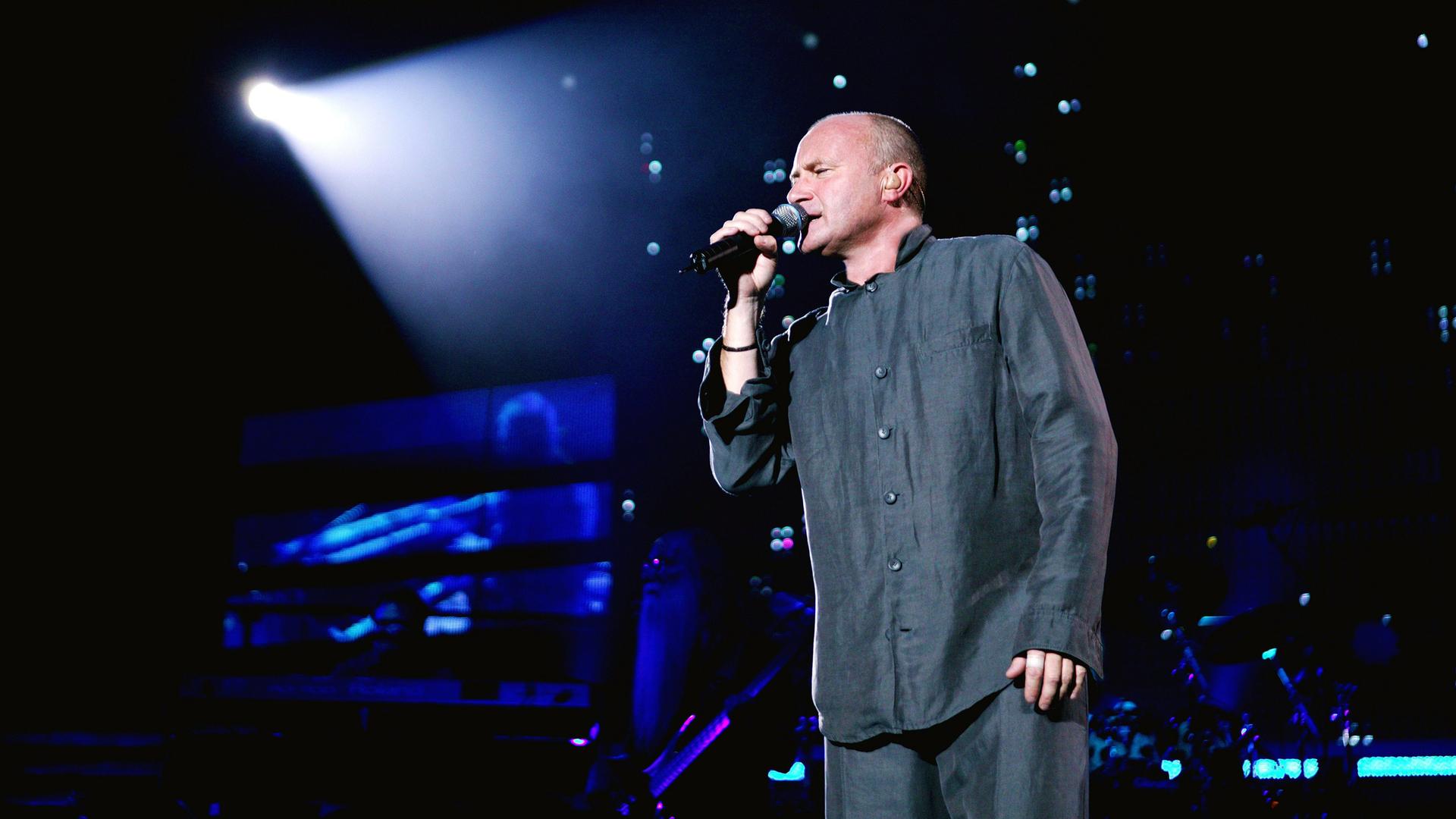 Phil Collins singt auf der Bühne in ein Mikro.