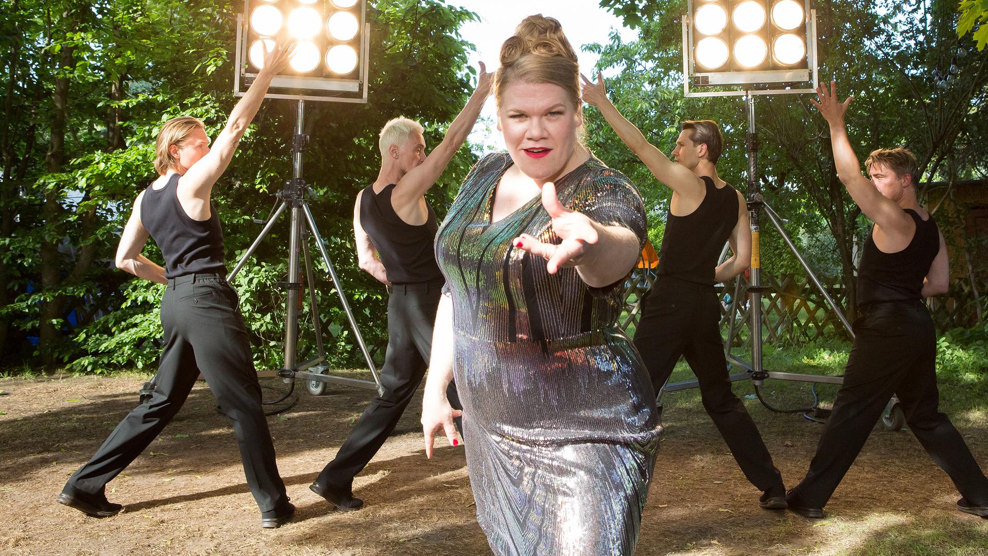 Dani Paschulke tanzt und singt im Bühnen-Outfit zusammen mit Tänzern vor dem Bauwagen