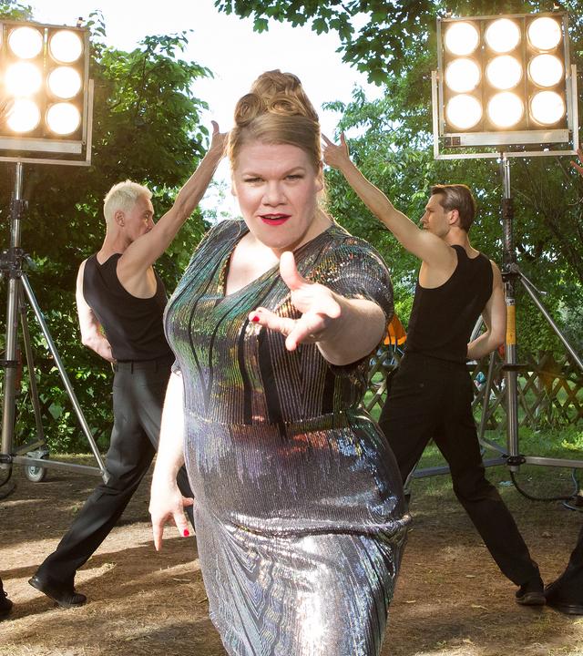 Dani Paschulke tanzt und singt im Bühnen-Outfit zusammen mit Tänzern vor dem Bauwagen
