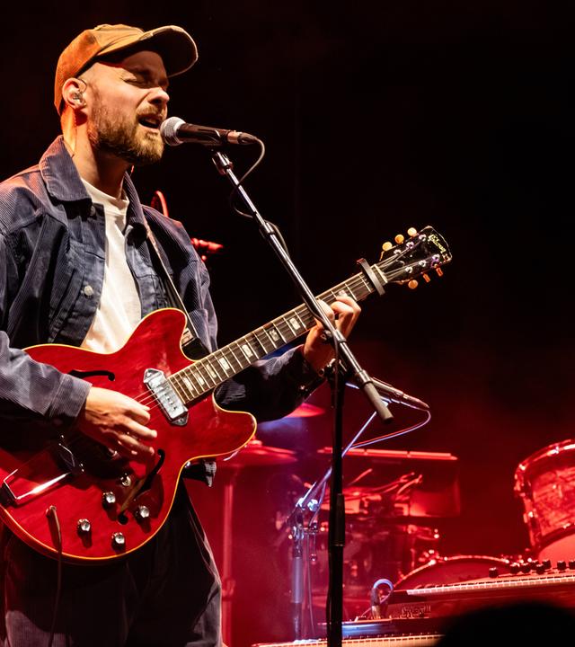Ein Mann, der Gitarre spielt, singt in ein Mikrofon.