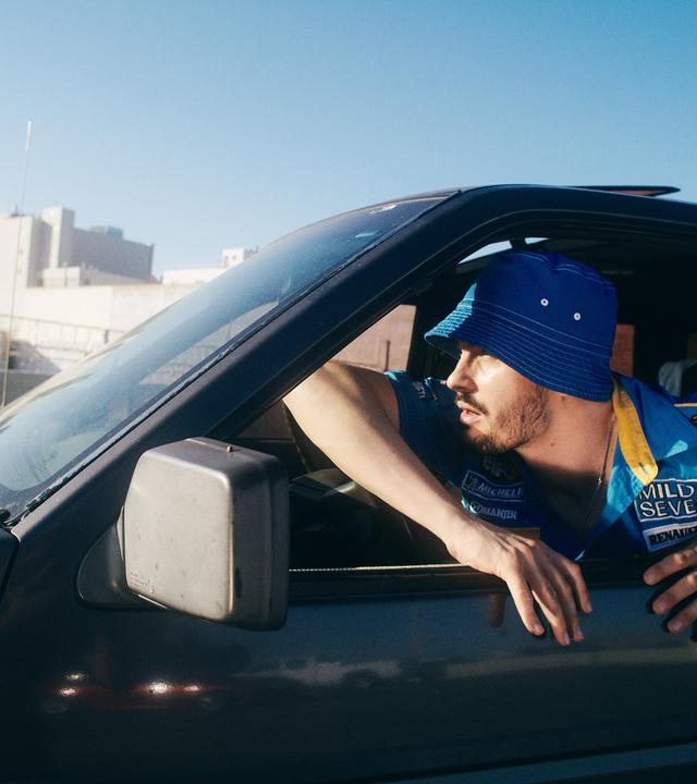 Ein Mann, der einen Hut trägt, schaut aus dem Autofenster an der Fahrerseite eines Auots.