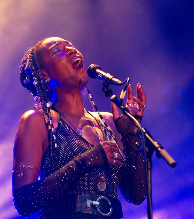 Eine schwarze Frau in glitzerndem Kostüm singt auf einer Bühne.