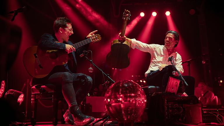 Zwei Männer posieren mit Gitarren auf einer Bühne.