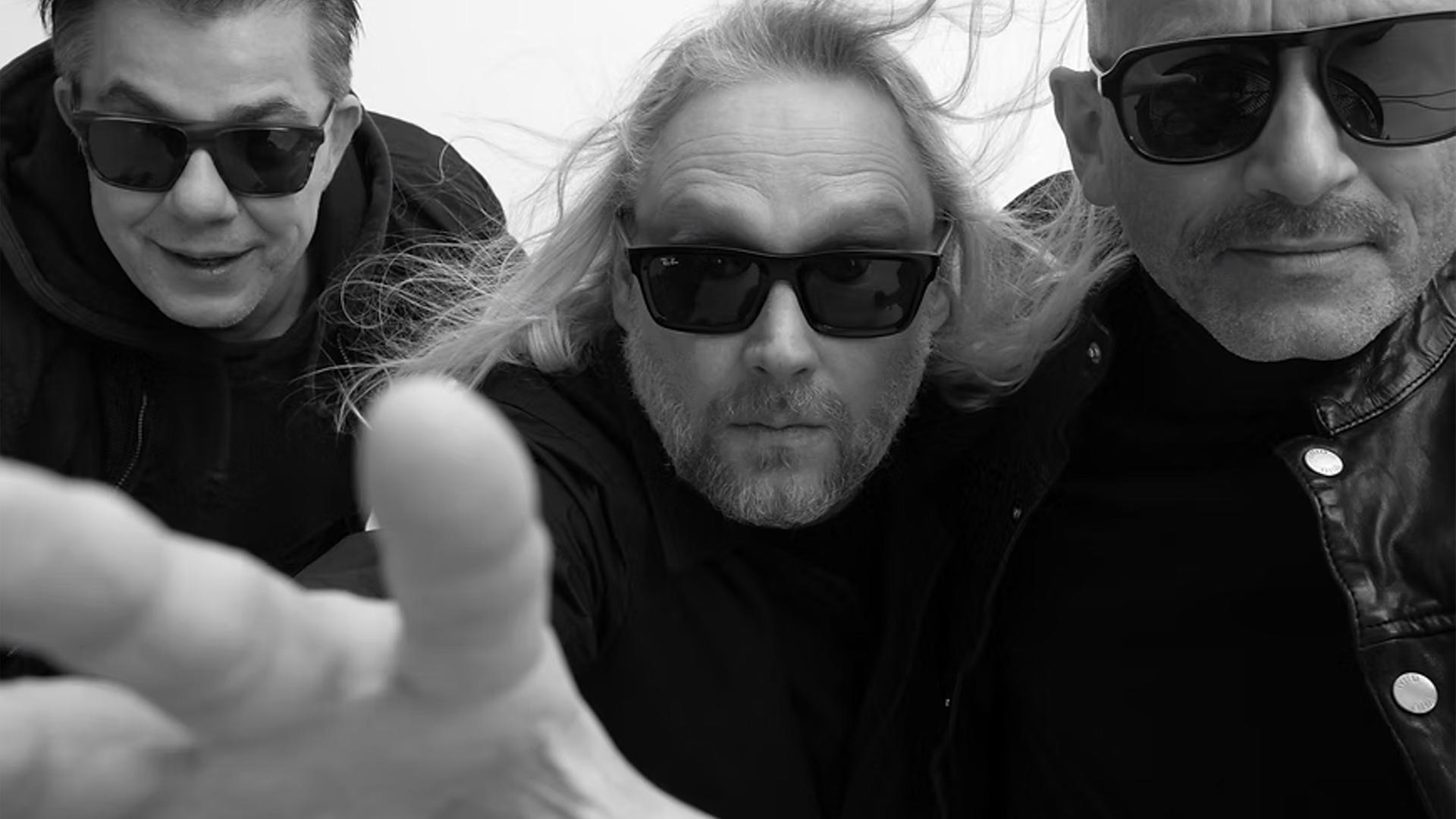 Die Schwarz-Weiß-Fotografie zeigt drei Männer, die Sonnenbrillen tragen.