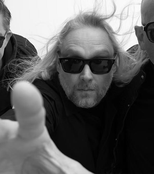 Die Schwarz-Weiß-Fotografie zeigt drei Männer, die Sonnenbrillen tragen.