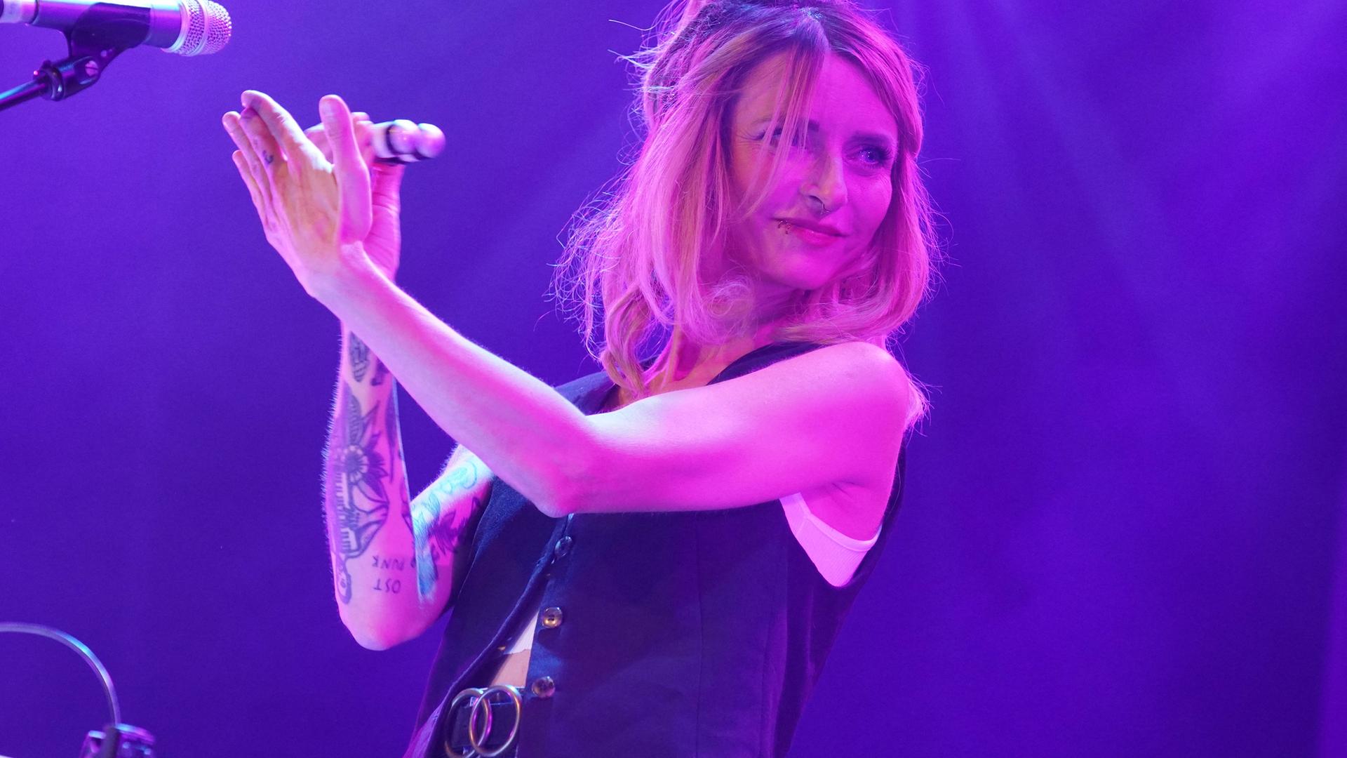 Eine Frau steht mit einem Musikinstrument in der Hand vor einem Mikrofon.