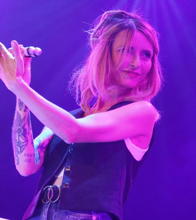 Eine Frau steht mit einem Musikinstrument in der Hand vor einem Mikrofon.