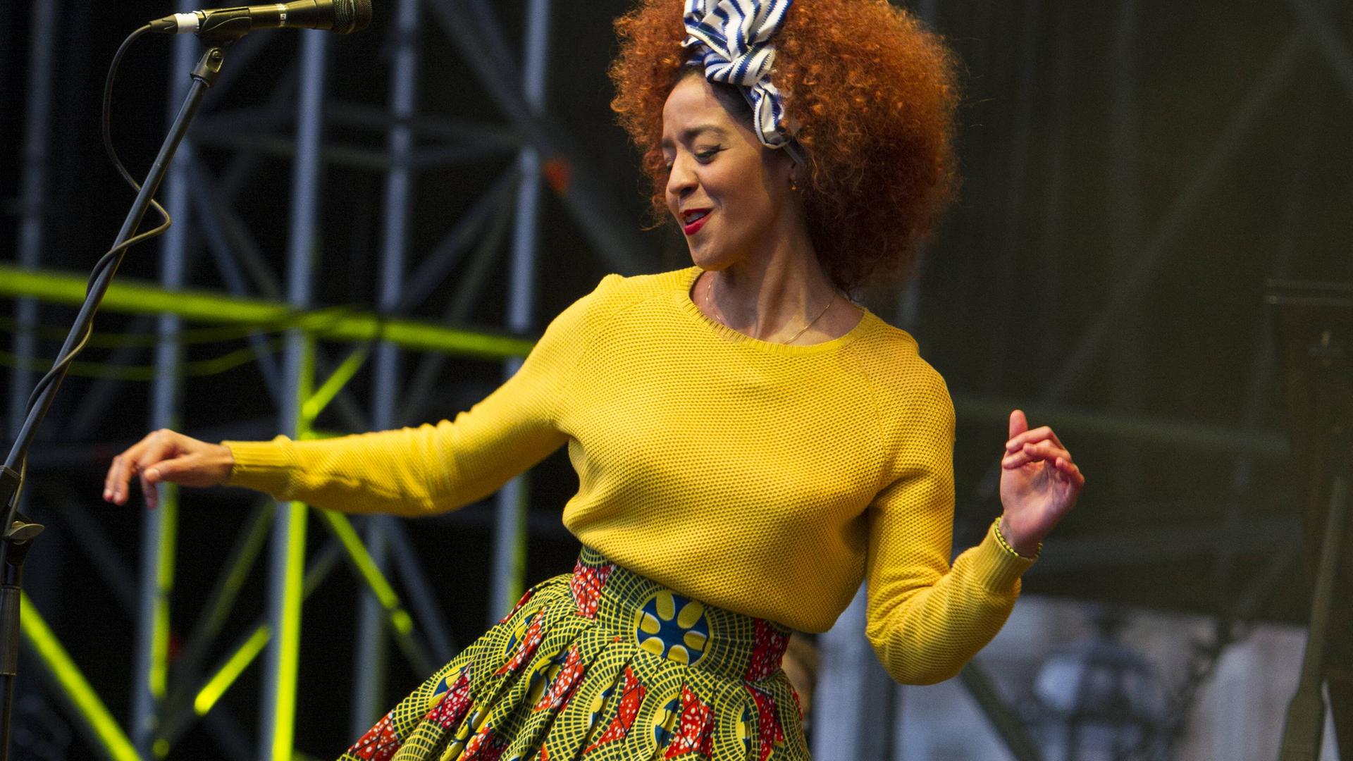 Eine Frau, die einen gelben Pullover trägt, tanzt auf einer Bühne.