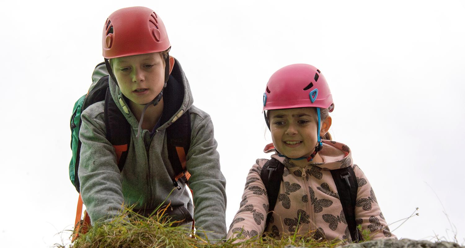 "Die Bergretter: Mutterliebe": Unterwegs in den Bergen, mit Rucksäcken und Wanderhelmen auf dem Kopf, knien Max (Nico Friesecke) und Mia (Mia-Sophie Ballauf) auf dem Boden und schauen ängstlich über einen Felsvorsprung in die Tiefe.
