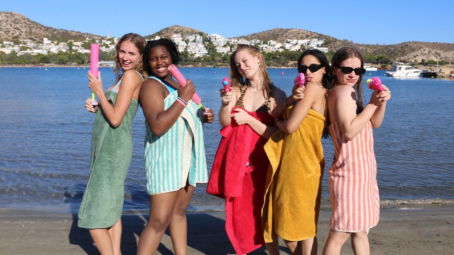 Nele, Faith, Johanna, Mahak und Josefine (v.l.n.r.) stehen am Strand. Jede hat ein Handtuch umgeworfen und eine Wasserpistole in der Hand.