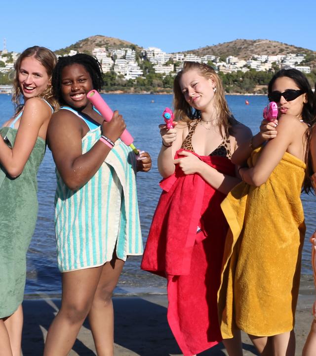 Nele, Faith, Johanna, Mahak und Josefine (v.l.n.r.) stehen am Strand. Jede hat ein Handtuch umgeworfen und eine Wasserpistole in der Hand.