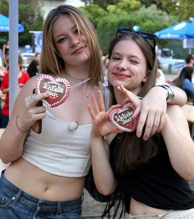 Johanna und Josefine stehen vor Holztischen auf einem Oktoberfest. Beide haben ein Lebkuchenherz um den Hals.