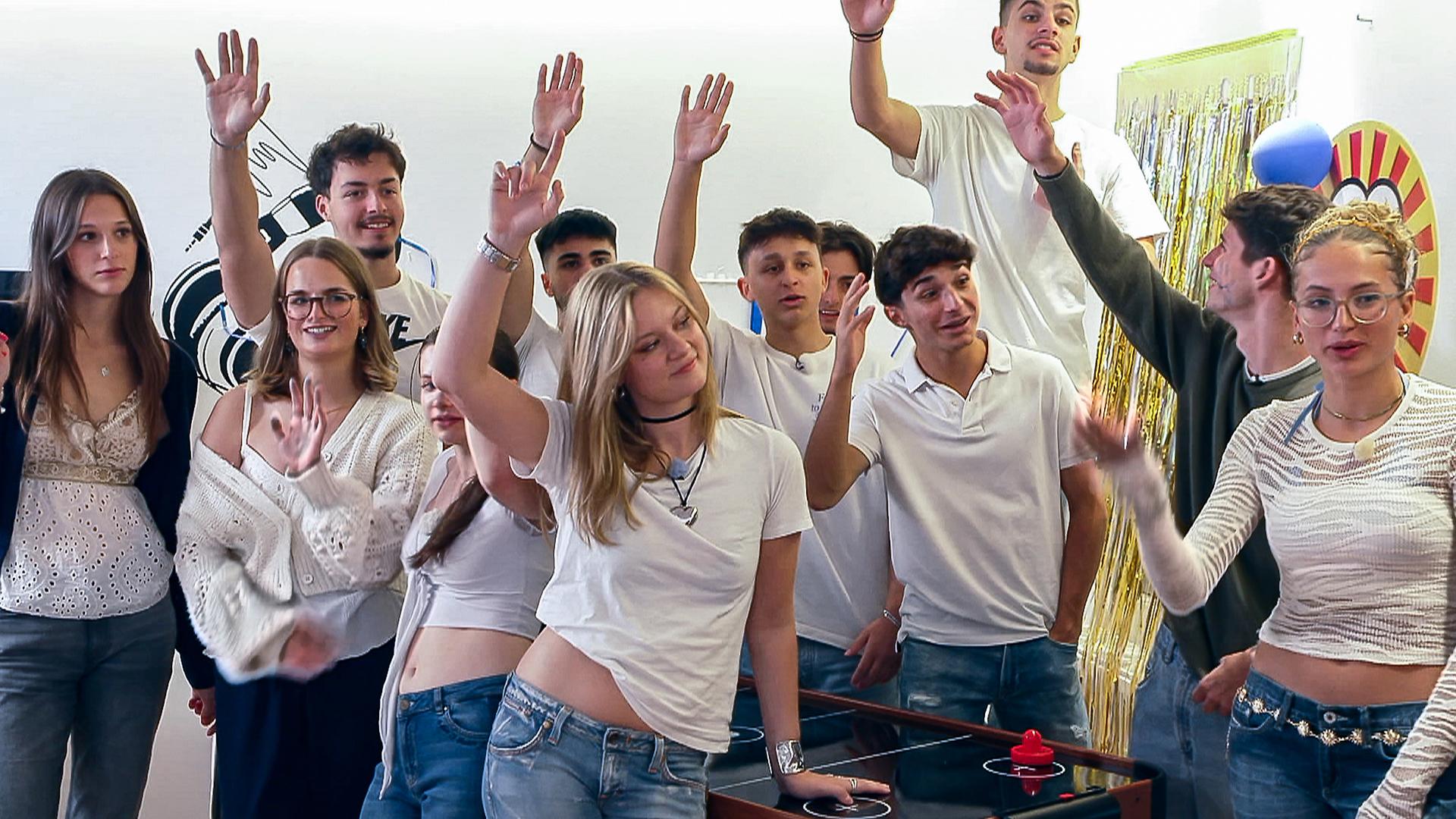 Johanna und Nele stehen umringt von Partygästen um einen Airhockey-Tisch. Viele im Bild halten ihre Hände in die Luft.