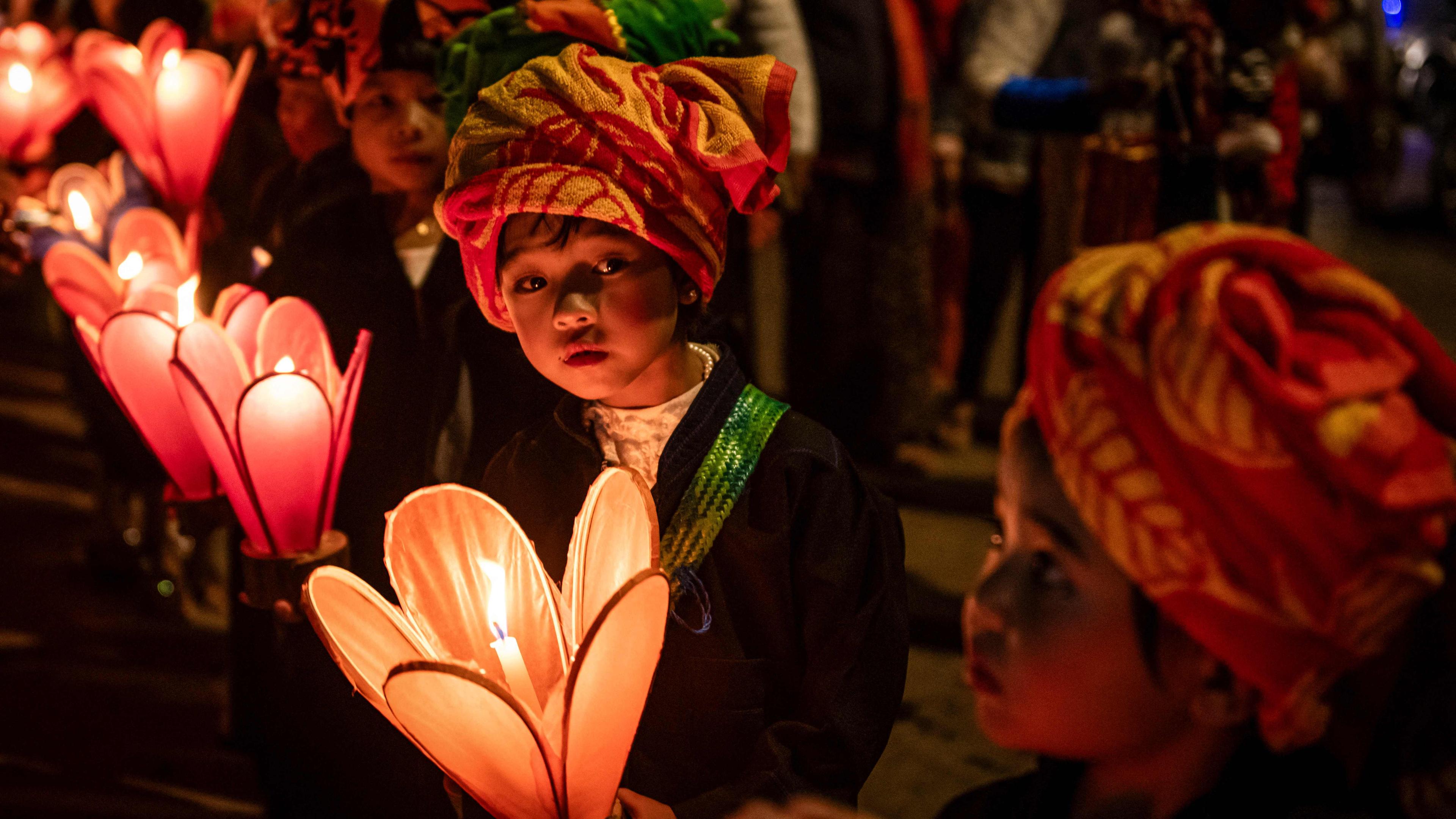 Kinder in Hüten sitzen im Dunkeln nebeneinander und halten Kerzenlichter Kerzenhaltern in Blumenform
