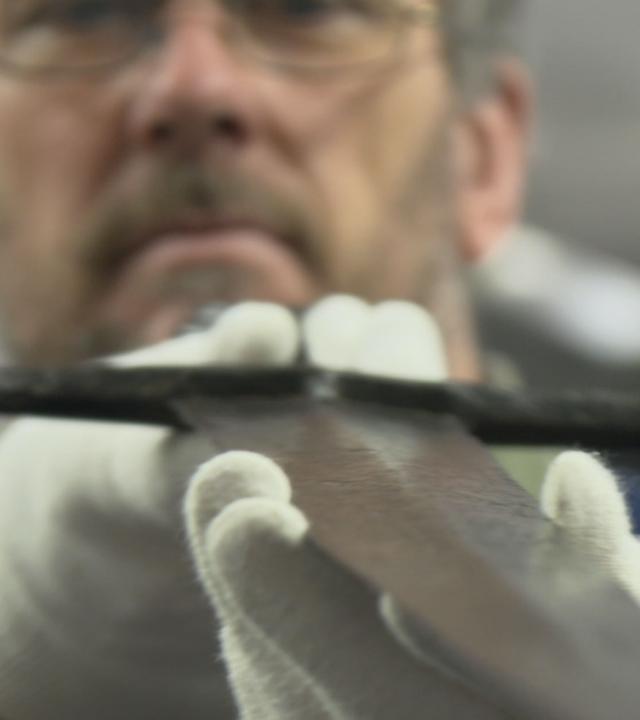 "Mysterien des Mittelalters - Die Schwerter von Castillon": Archäologe Tim Sutherland untersucht ein Castillon-Schwert, Sammlung der Royal Armouries, Leeds, England - hält das Schwert vor sich, prüft die Klinge.