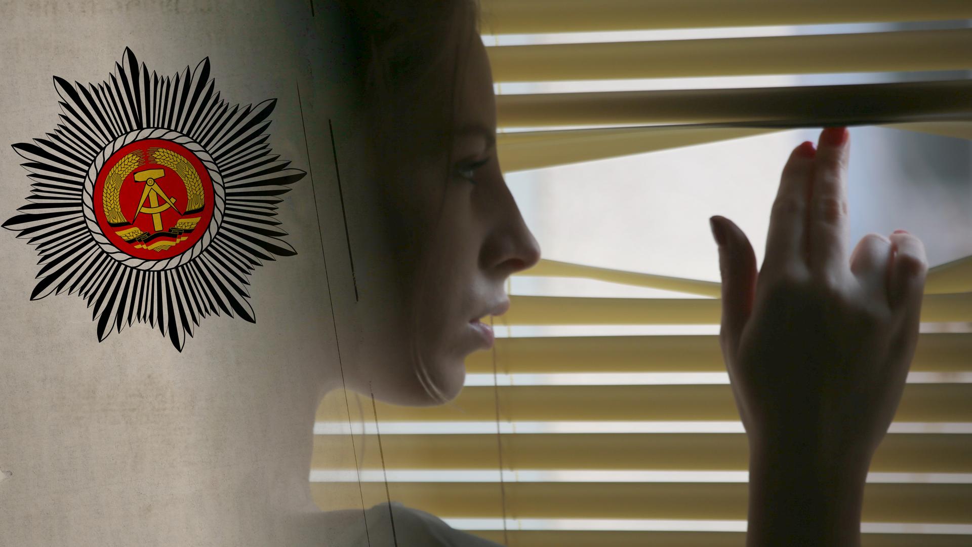 Eine Frau blickt verstohlen durch die Jalosien nach draußen.