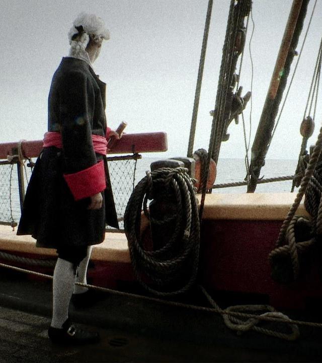 "Mythen-Jäger: Der Piratenschatz des Capttain Kidd": Ein Mann steht auf einem Schiff und blickt in die Ferne. Er hat ein Fernrohr in der Hand, blickt jedoch nicht durch.