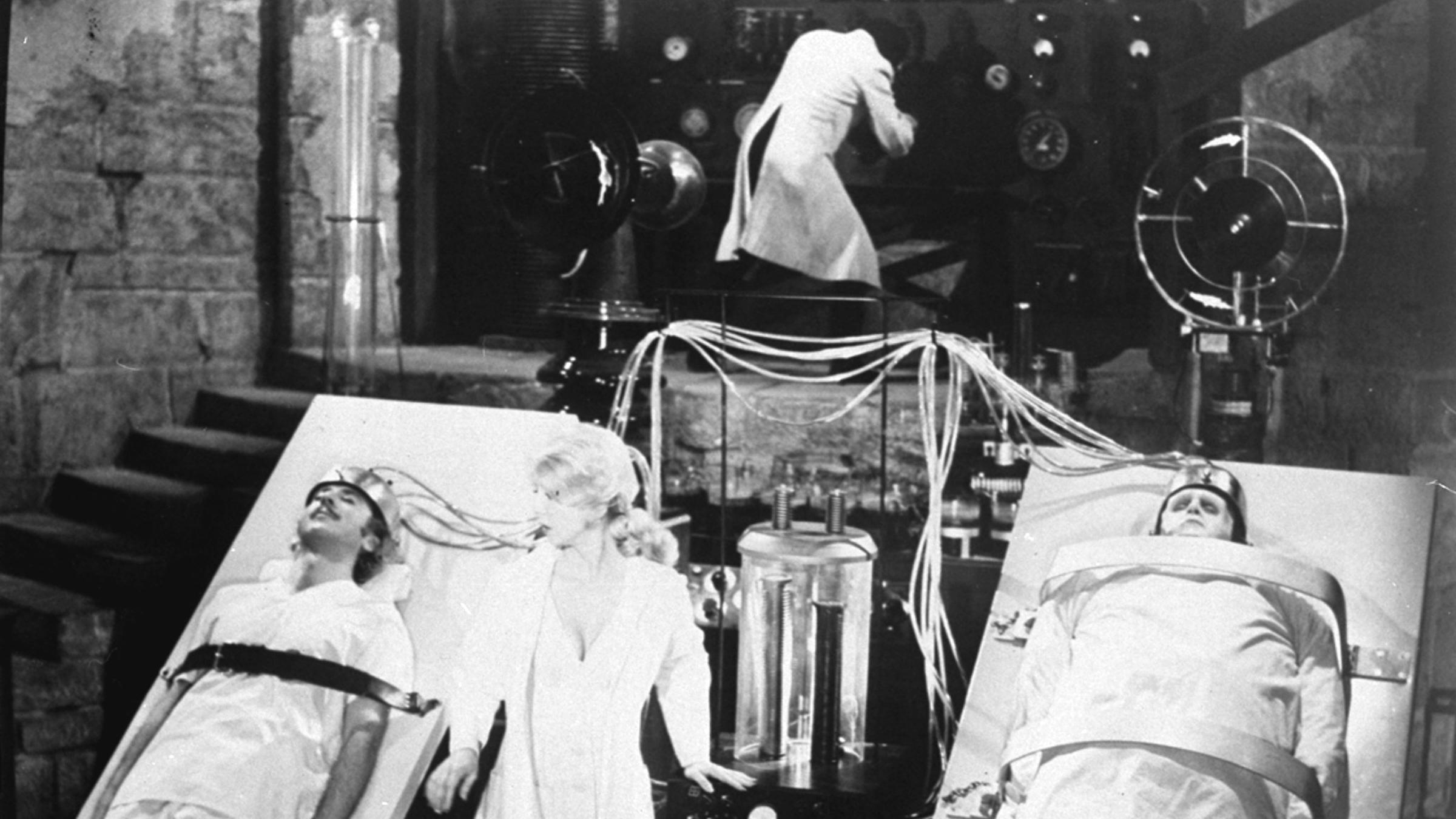 "Mythos - Die größten Rätsel der Geschichte: Frankenstein": schwarzweiße Laborszene aus "Frankenstein Junior". Die Organe von jungem Dr. Frankenstein, gespielt von Gene Wilder, links,  werden durch die des Monsters, gespielt von Peter Boyle, rechts, ausgetauscht. Dazwischen steht eine Frau im weißen Kittel. Oben ist ein Wissenschaftler zu sehen. 