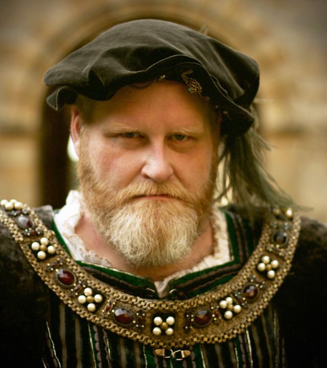 Spielszene. Porträt Heinrich VIII. mit rotblond graumeliertem Vollbart. Er trägt ein dunkelgrünes Samtbarett mit Feder und Brosche sowie einen dunklen Überrock im Renaissancestil.