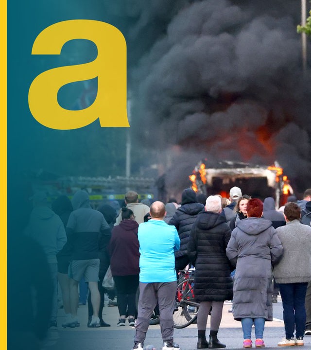 Große Rauchwolke über brennendem Auto in einer Straße in Belfast, davor Menschenmenge