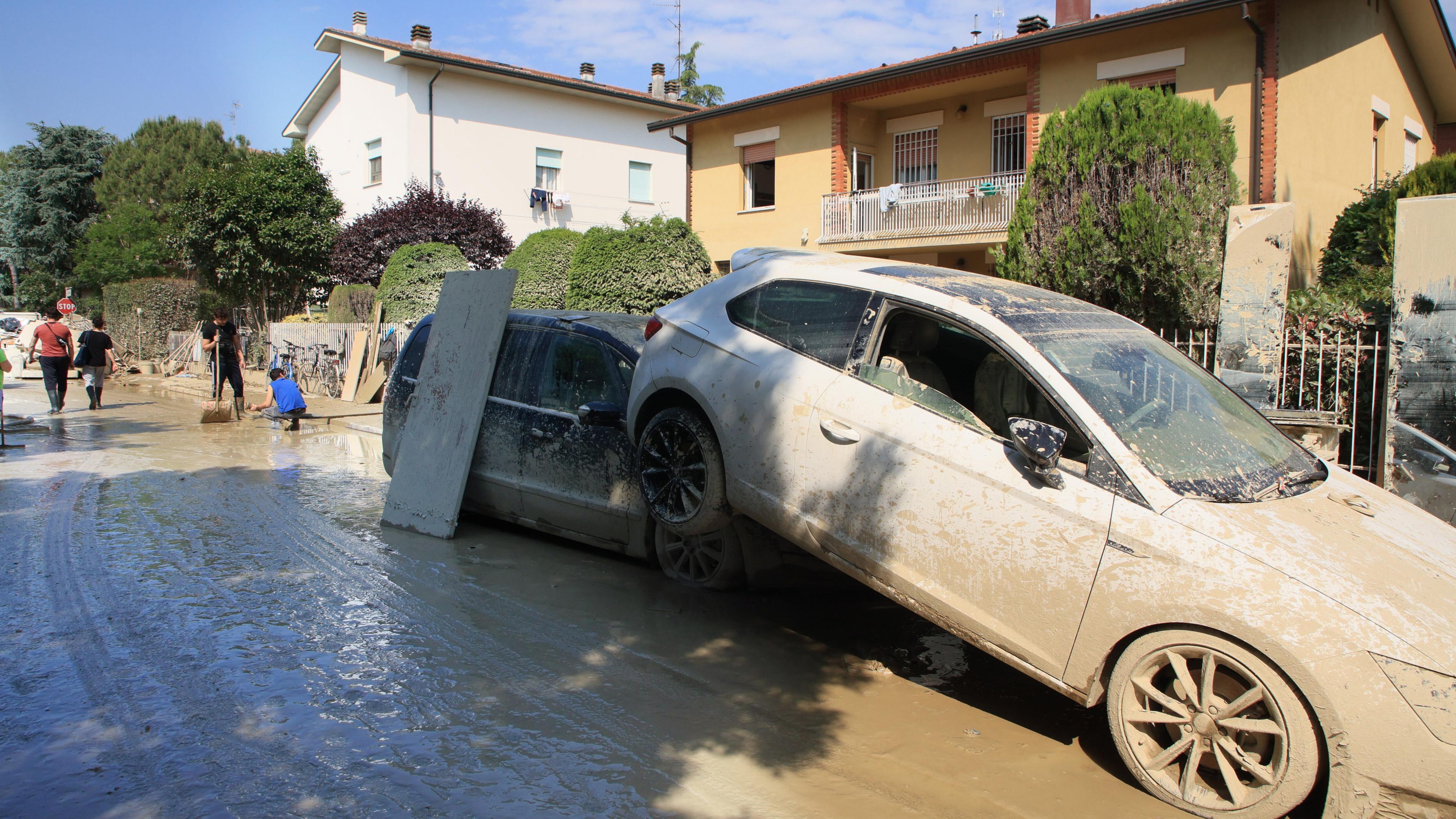 Menschen beseitigen Schutt und Schlamm von der Straße, der durch das Hochwasser angespült wurde, während neben ihnen durch das Hochwasser beschädigte Autos zu sehen sind.
