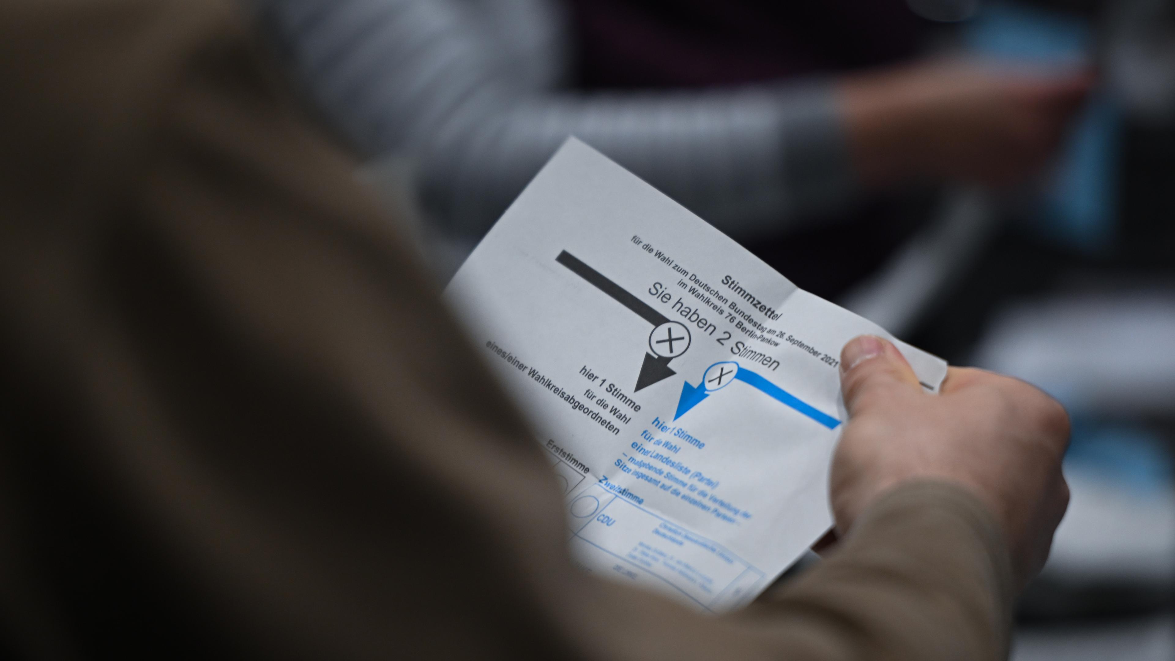Ein Wahlhelfer hält während der Auszählung der Briefwahlstimmen in der Max-Schmeling-Halle einen Stimmzettel in der Hand.