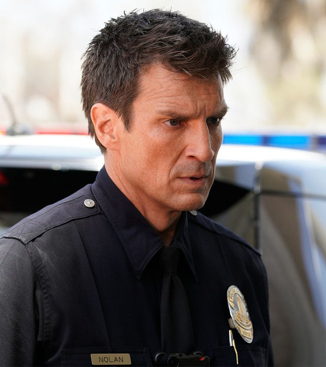 "The Rookie - Nachtschatten": John Nolan (Nathan Fillion) schaut mit entschlossenem Blick in die Ferne. Im Hintergrund ist ein Polizeiauto zu sehen.