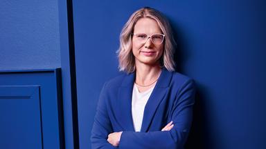 ZDF-Programmdirektorin Nadine Bilke steht in einem blauen Anzug vor einer blauen Wand und schaut mit verschränkten Armen lächelnd in die Kamera