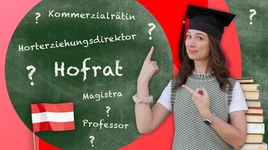 Vor einer Tafel mit Begriffen wie „Hofrat“, „Professor“ und „Magistra“ zeigt Julia Nestlen mit Doktorhut auf traditionelle österreichische Titel und Statusbezeichnungen.