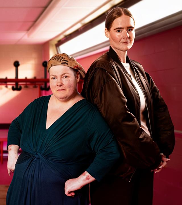 Zwei Frauen (Natalie Rosenke und Alina Friedrichs) stehen, die Rücken aneinander angelehnt, in einer Umkleidekabine.