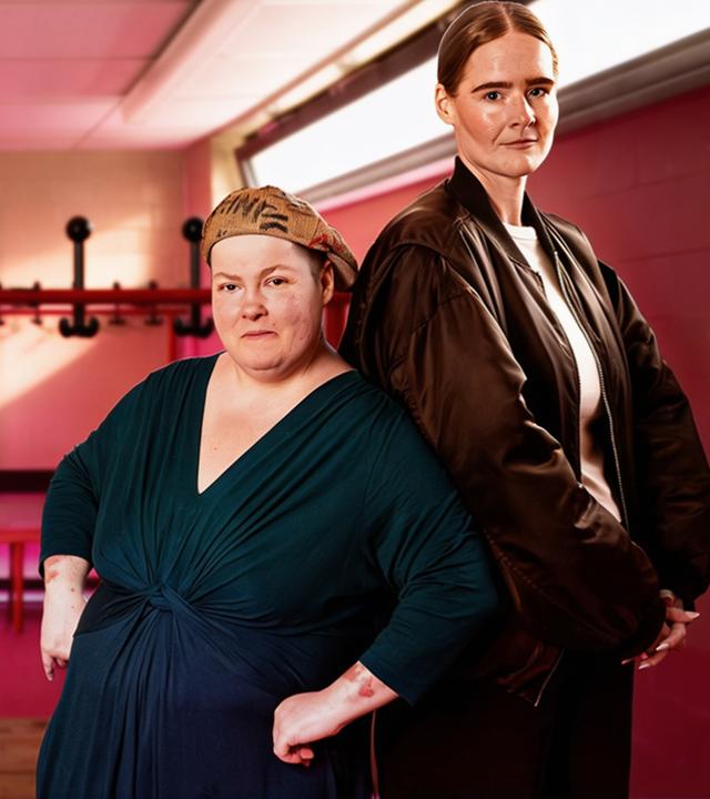 Zwei Frauen (Natalie Rosenke und Alina Friedrichs) stehen, die Rücken aneinander angelehnt, in einer Umkleidekabine.