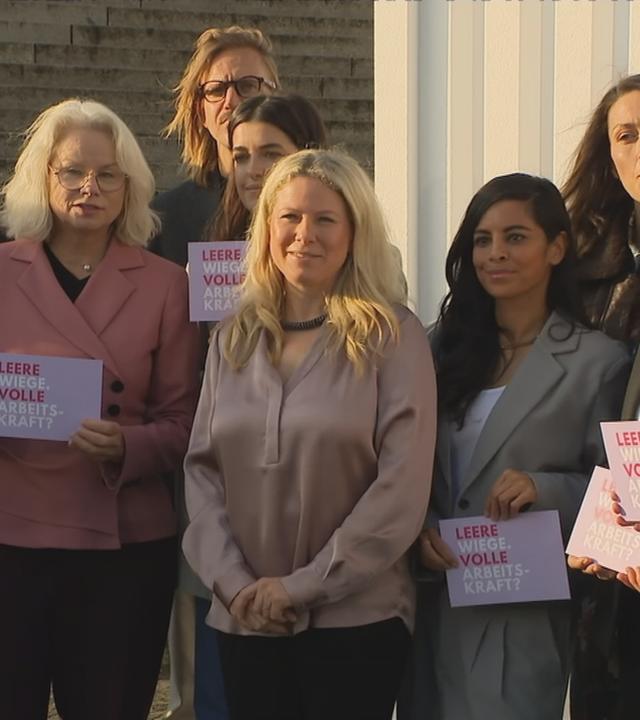 Frauen stehen in einer Reihe und halten Schilder hoch mit der Aufschrift "Leere Wiege, volle Arbeitskraft?"