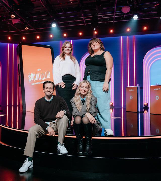 Marti Fischer, Caro Worbs, Laura Larsson und Teresa Reichl (v.l.n.r.) posieren zusammen im Studio der ZDFneo-Gameshow "Neo Social Club". Hinter ihnen im Studio steht ein überdimensionierter Smartphone-Bildschirm.