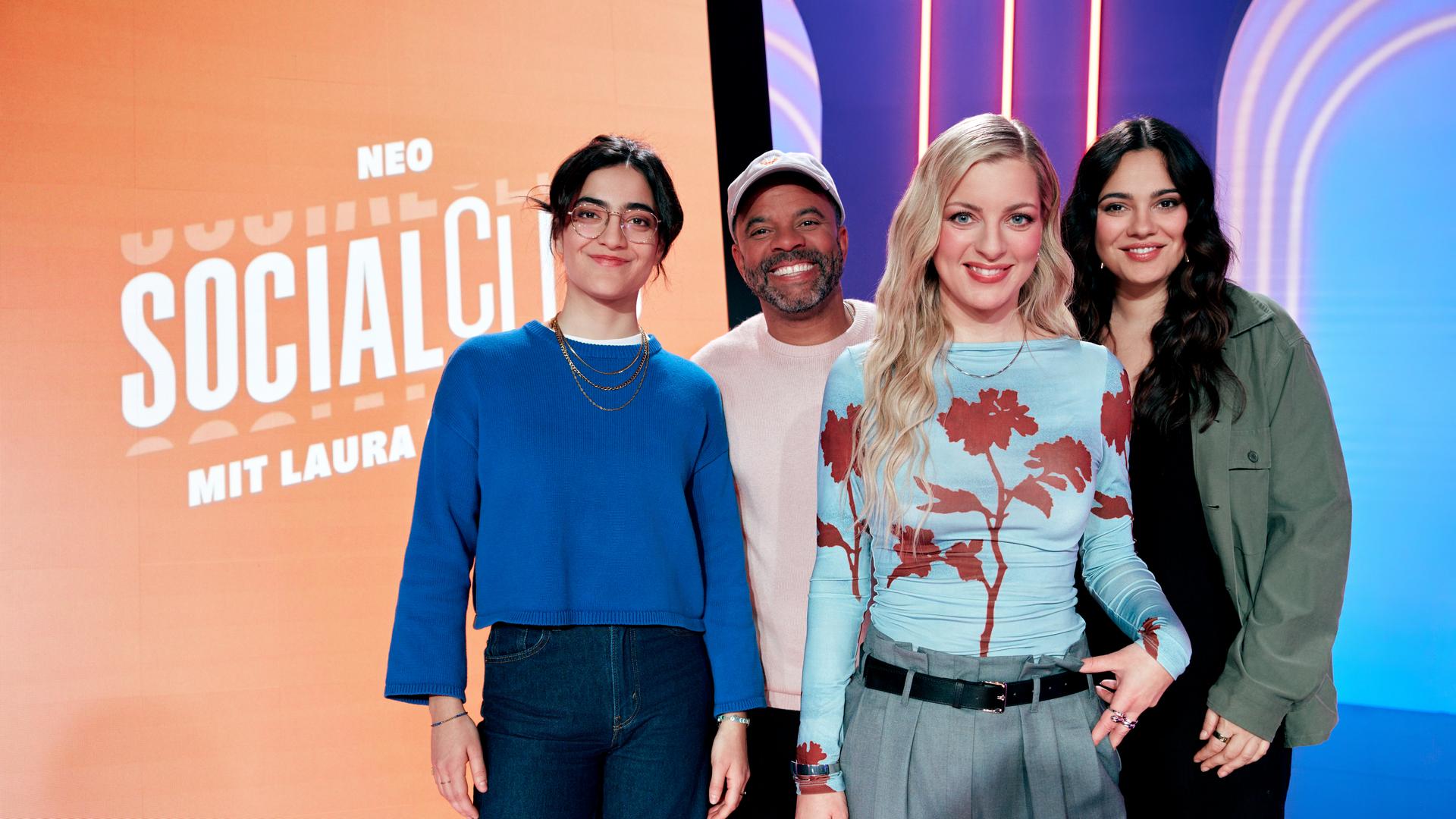Ana Lucía. Simon Pearce, Laura Larsson und Nilam Farooq (v.l.n.r.) stehen im Studio des Formats "Neo Social Club". Hinter ihnen steht ein großer Bildschirm, auf dem das Logo der Sendung eingeblendet ist. 